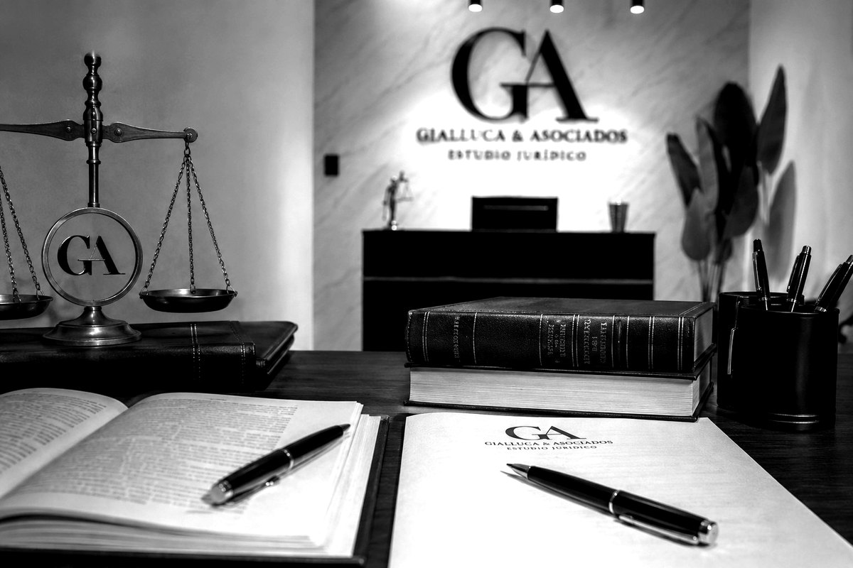 Escritorio del Estudio Jurídico Gialluca & Asociados con balanza, libros de derecho y el logo GA en la pared